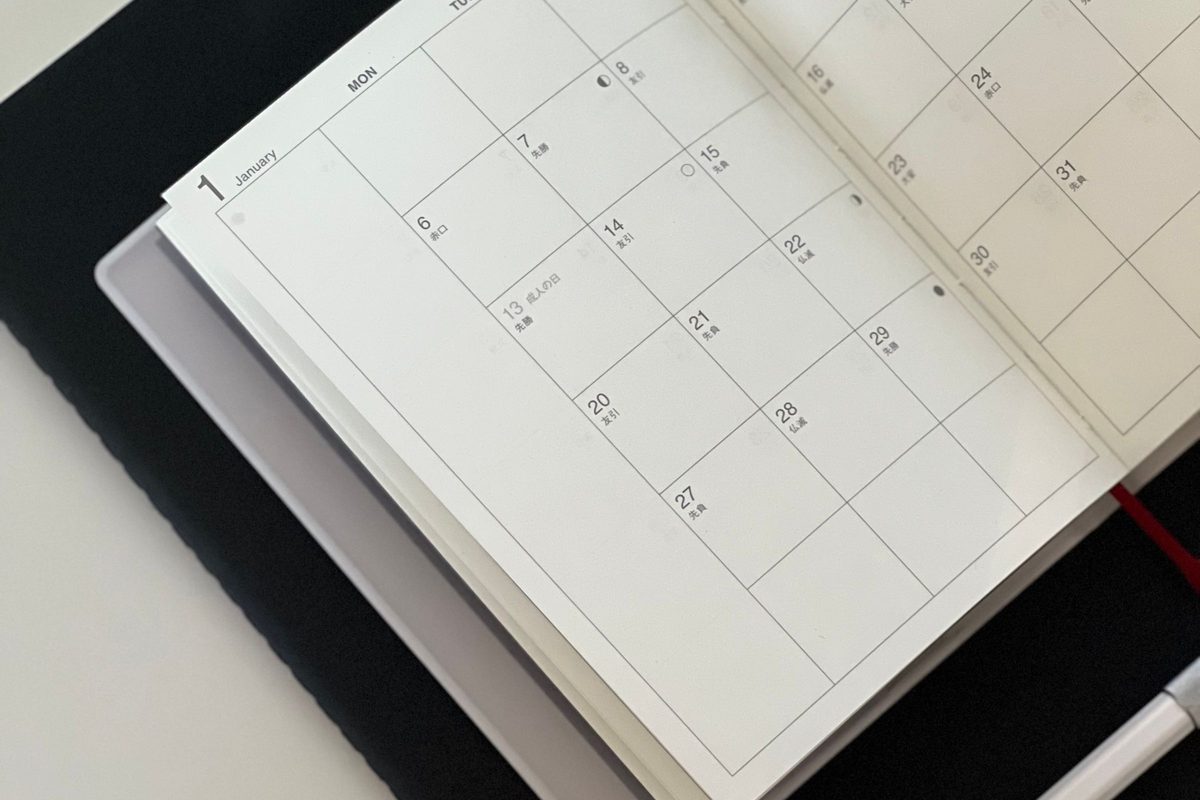 An open monthly planner and a pen on a dark desk.