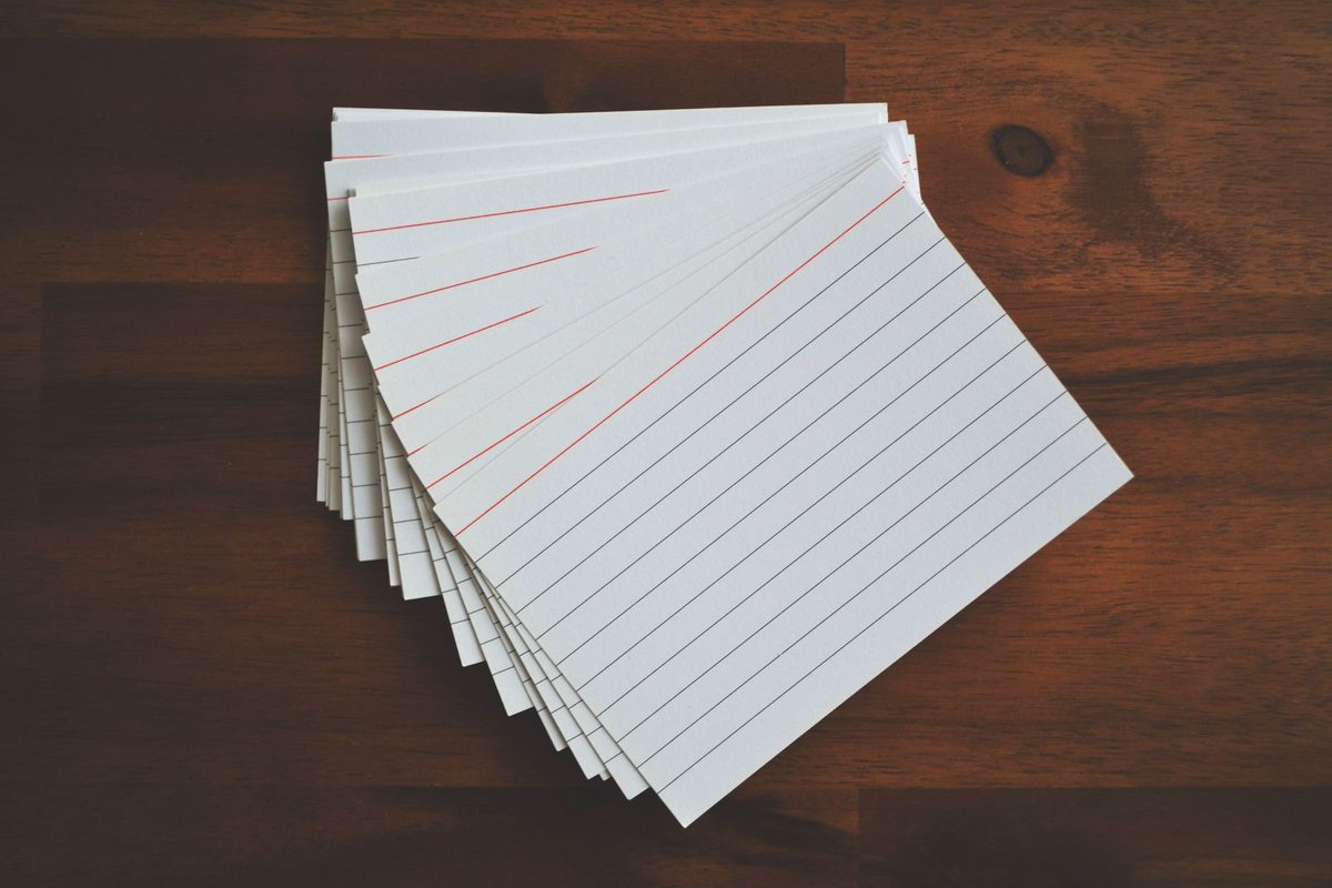 A fanned stack of blank index cards on a dark wooden desk.