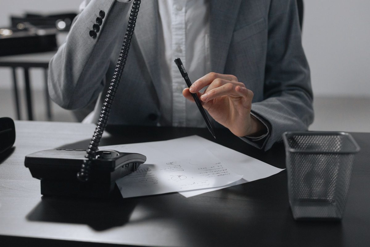 A person on a desk phone call taking notes with a pen, face out of frame.